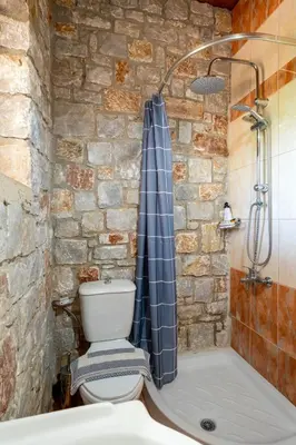a stone walled bathroom with a toilet and a shower at Villa Kamaraki in Patellárion