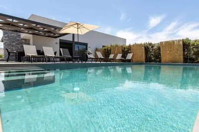 a large swimming pool with chairs and an umbrella at Diktamos Villa by Vintage Travel in Tavronitis