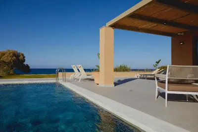 a swimming pool with chairs and the ocean in the background at Giannoulis Ele Villas in Skoutelónas