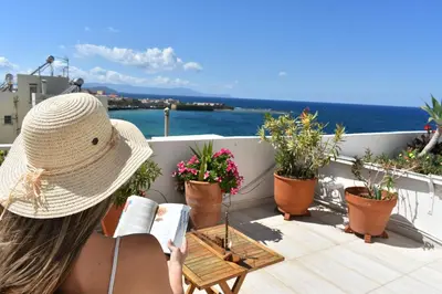 a woman reading a book on a balcony with plants at Diotima - Astonishing seaview apartment in Chania Town