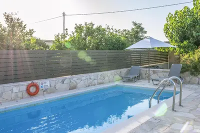 a swimming pool with a fence and an umbrella at Villa Rouga by Andrian Villas in Kalamítsion Alexándrou