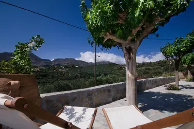 a table and chair with a tree and mountains in the background at Kallimento-Dimitra in Kissamos