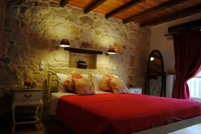 a bedroom with a red bed with a stone wall at Rock House's Villa Melody in Plataniás