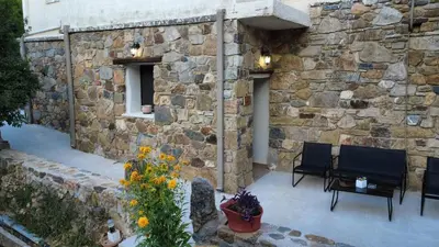 a stone wall with two chairs and a table and flowers at Petra Homes Temenia in Teménia