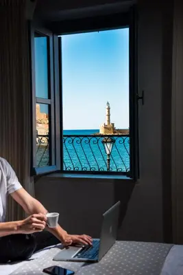a person sitting on a bed with a laptop and a window at Elia Zampeliou Hotel in Chania Town