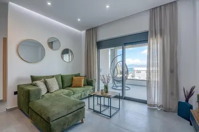a living room with a green couch and a large window at Gems - Stunning 2BR Apts - Steps from the Beach! in Kissamos