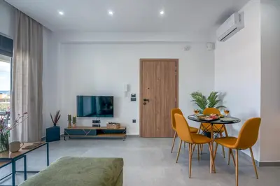 a living room with a table and chairs and a television at Gems - Stunning 2BR Apts - Steps from the Beach! in Kissamos