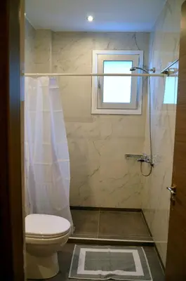 a bathroom with a shower with a toilet and a window at Tile Apartments 6 in Agia Marina Nea Kydonias