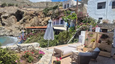 a patio with an umbrella and chairs and flowers at Sfakia On the Beach in Khóra Sfakíon