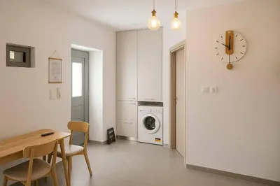 a kitchen with a table and a washing machine and a clock at Yalos Standard Studio - 5 mins to Elafonisi beach in Agios Padeleimon
