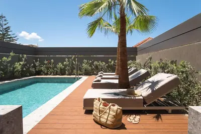 a pool with chaise lounges and a palm tree at Memoire Guest House I Private Heated Pool I 200m beach in Chania Town