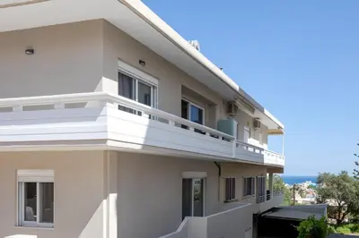a white building with balconies and the ocean in the background at Artemis Apartments in Chania Town