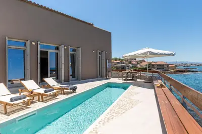 a pool with chairs and an umbrella next to a house at Kormoranos-Hydrobates Waterfront Villa in Chania Town