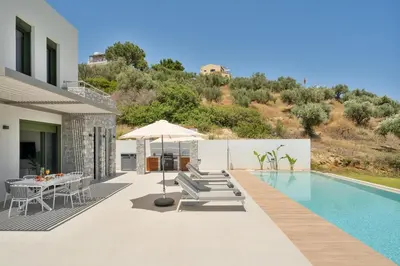 a villa with a swimming pool with chairs and an umbrella at Villa Meraki in Stalos