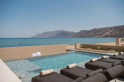 a swimming pool with chaise lounge chairs and the ocean at Onora Villa - Steps from the Sea by etouri in Nopíyia