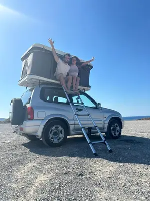 two people sitting on the roof of a car at Rooftop Jeep Escape Sleep Under the Stars in Chania Town