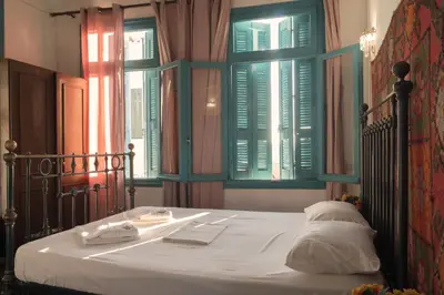 a bedroom with a bed with white sheets and windows at Pension Nora in Chania Town