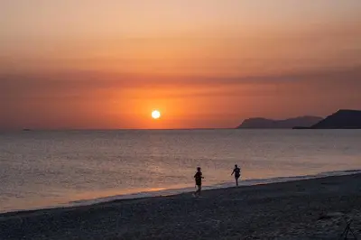 two people walking on the beach at sunset at Gemini Villas Chania - Calma & Siesta in Maleme