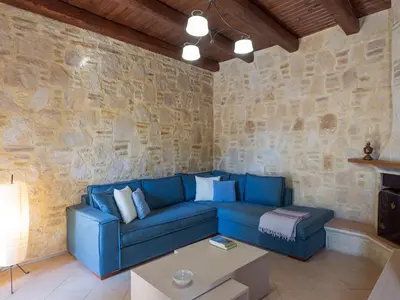 a living room with a blue couch and a stone wall at 3-Min Drive to Kalyves Beach, Stone Home with Private Pool in Armenoi Center in Arménoi