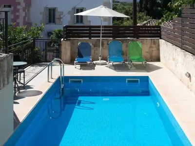 a swimming pool with two chairs and an umbrella at 3-Min Drive to Kalyves Beach, Stone Home with Private Pool in Armenoi Center in Arménoi