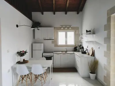 a kitchen with white cabinets and a table and chairs at Villa Naiades Traditional Cretan Stone House with private Pool and Garden in Chania in Arménoi