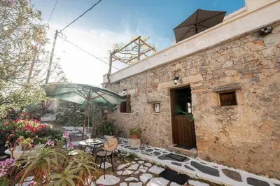 a stone building with a table and chairs and an umbrella at Agapi's Charming Retreat - Rustic Escape in Chania in Maláxa