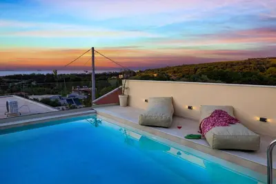 a swimming pool with pillows on a balcony with a sunset at Villa Metochi with Private Pool in Palio Gerani