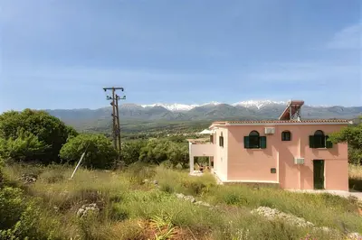 a pink house in a field with mountains in the background at 5-bedroom Country House in Crete - Olive Grove Retreat in Nerokhórion