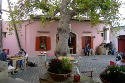 a pink building with people sitting at tables under a tree at Villa Rodi in Gavalochori