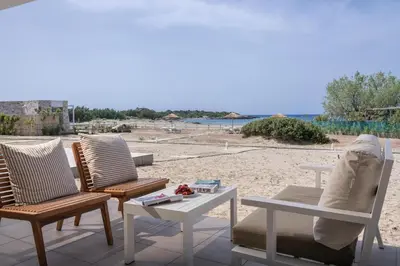 two chairs and a table on a patio with a beach at Cedar Bay Beachside Villas in Palaiochóra