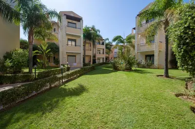 a yard in front of a building with palm trees at Creta Palm Resort Hotel & Apartments in Stalos