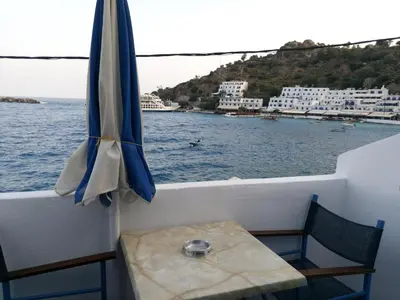 a table and an umbrella on a balcony next to the water at Faros Rooms in Loutro