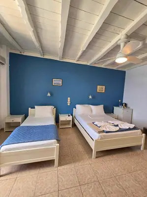 two beds in a room with a blue wall at Faros Rooms in Loutro