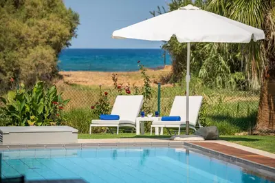 two chairs and an umbrella next to a swimming pool at Blue Sea Luxury Villa in Maleme