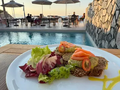 a plate of food on a table next to a pool at Τhe Noverian Antama Organic Beach Resort Chania with Outdoor Heated Pool in Agia Marina Nea Kydonias