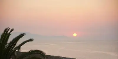 a sunset over the ocean with a palm tree at Villa Alexander in Kalathas