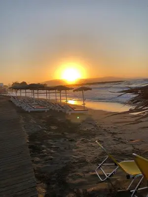 a sunset on a beach with chairs and umbrellas at Margarita Beach Hotel in Agia Marina Nea Kydonias