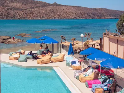a pool with chairs and umbrellas next to the water at Chrispy Beach Resort, Agia Marina in Agia Marina Nea Kydonias
