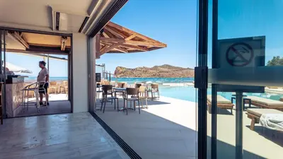 a man standing on a patio with a view of the ocean at Chrispy Beach Resort, Agia Marina in Agia Marina Nea Kydonias
