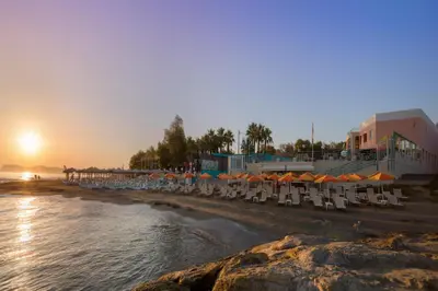 a beach with chairs and umbrellas at sunset at Chrispy Beach Resort, Agia Marina in Agia Marina Nea Kydonias