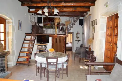 a living room with a table and chairs and a room with a staircase at Stone Mansion in Káïna