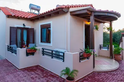 a small white house with a porch and potted plants at Kyriaki's Cozy Apartments in Agia Marina Nea Kydonias