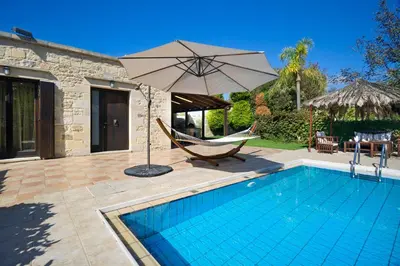 a pool with a hammock and an umbrella next to a house at Cozy Stone Villa in Plátanos