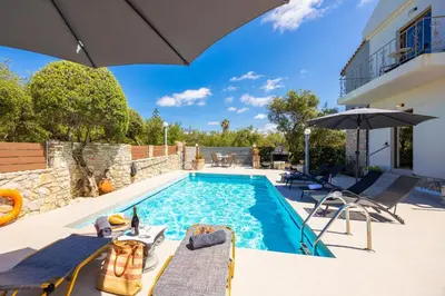 a pool with chairs and an umbrella next to a house at Villa Tzina in Plataniás