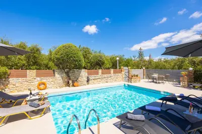 a swimming pool with chairs and umbrellas in a backyard at Villa Tzina in Plataniás