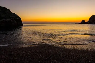 a sunset on a beach with rocks in the water at Villas Paleochora in Palaiochóra