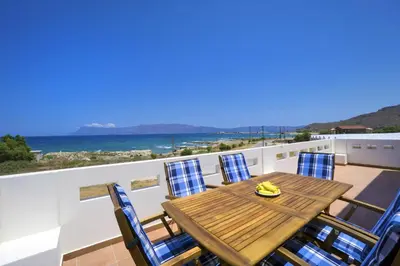 a wooden table and chairs on a balcony with the ocean at Seaside Villa Balos in Kissamos