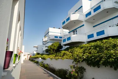 a white building with blue windows and a sidewalk at Hotel Mimoza in Agia Marina Nea Kydonias