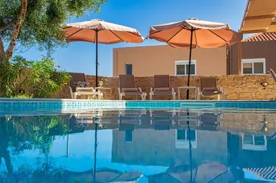 two umbrellas and chairs next to a swimming pool at Theo Villas With Sea View in Marathokefála
