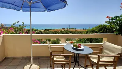 a table and chairs on a balcony with an umbrella at Doma Apartments in Falasarna